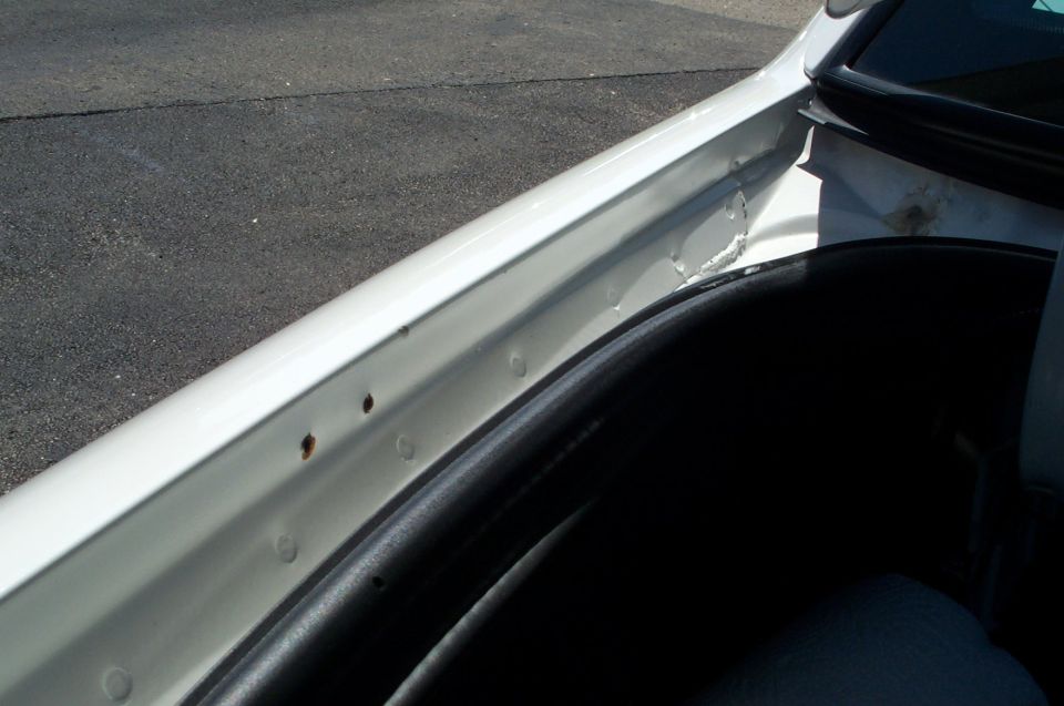 White door jamb of a Crown Victoria with small rust spots and paint blemishes, door open showing black trim