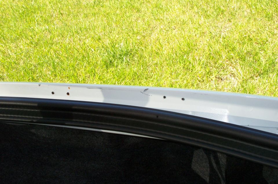 Gray trunk opening edge with black seal and grass background. Supermotors logo visible
