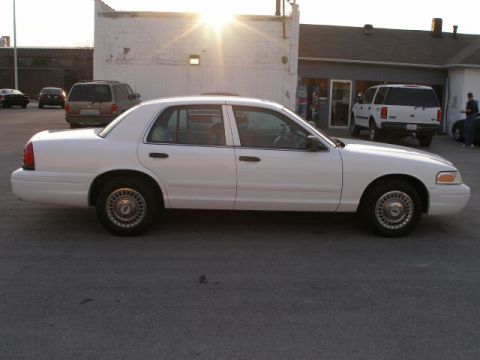 2001 Ford Crown Victoria - A white 2001 Ford Crown Victoria is parked outside a building with other vehicles visible.