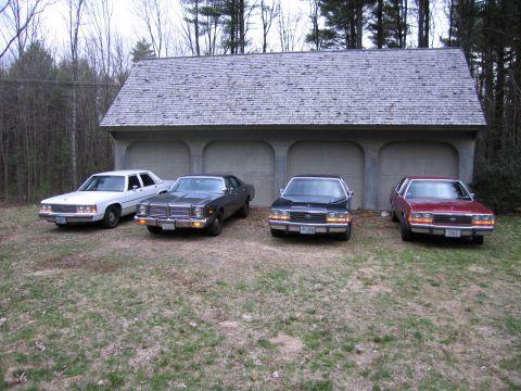 1991 Ford LTD Crown Victoria - Four sedans are parked in front of a garage with a shingled roof.