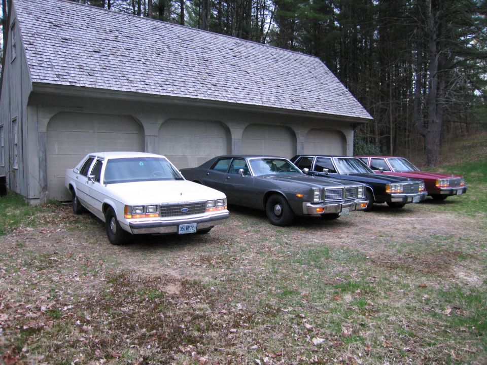 Four sedans parked in front of a garage: a white Ford, a dark gray sedan, a dark blue sedan, and a red sedan
