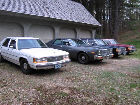 1991 Ford LTD Crown Victoria - A line of four sedans, appearing to be from the 1980s, are parked in front of a garage.