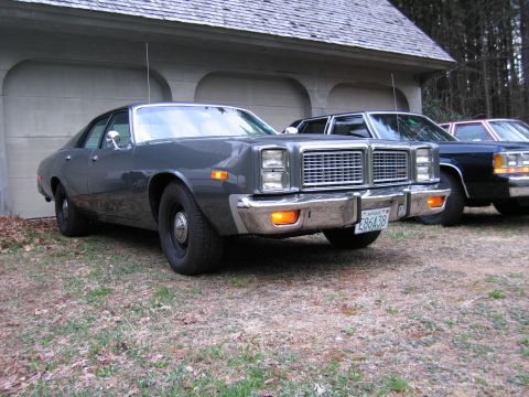 1991 Ford LTD Crown Victoria - A gray sedan with a prominent chrome grille and bumper is parked in front of a garage, with other vehicles visible behind it.