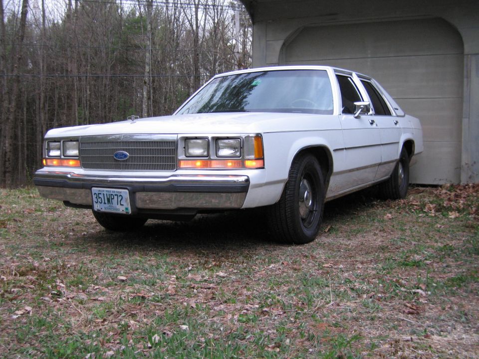 White sedan parked in front of a garage, front 3/4 view. License plate reads 351WP72