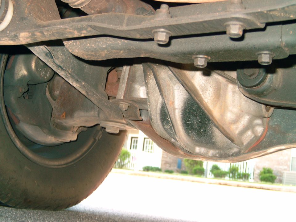 Underside view of a vehicle's rear axle and suspension components. Shows the differential housing, driveshaft, and part of the tire