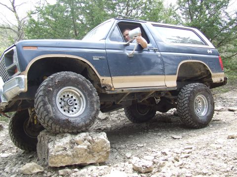 1986 Ford Bronco - This blue 1986 Ford Bronco is shown navigating a rocky trail, demonstrating its off-road capabilities.