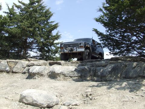 1986 Ford Bronco - A Ford Bronco navigates a rocky terrain under a clear blue sky.