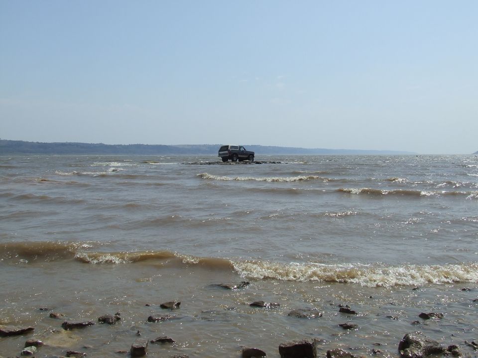 Ford Bronco parked on rocks in shallow water with waves
