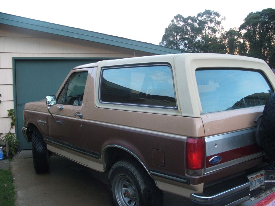 Brown and tan Ford Bronco parked beside a green garage door, side and rear view