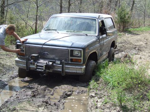 1986 Ford Bronco - A 1986 Ford Bronco is stuck in a muddy trail, its front winch visible.