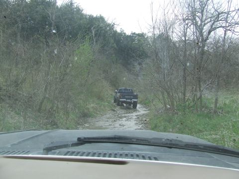 1986 Ford Bronco - Toyota pickup truck navigates a rough dirt road surrounded by trees.
