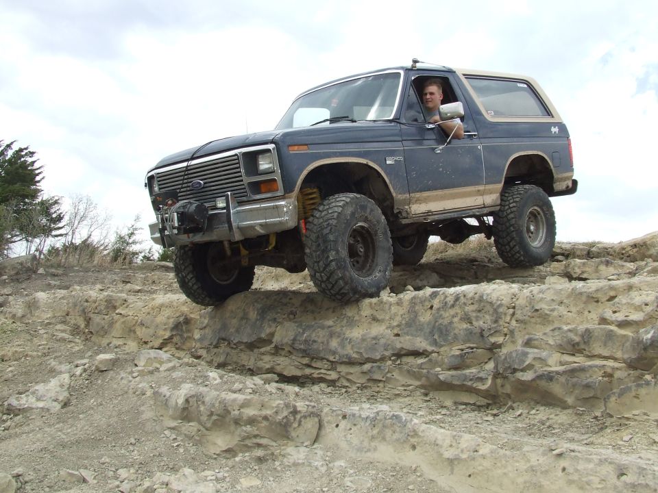 Dark blue Ford Bronco with lifted suspension and large tires driving over rocks