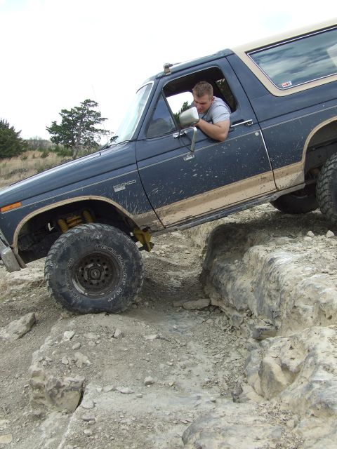 1986 Ford Bronco - A man drives a dark blue Ford Bronco off-road, navigating a rocky terrain.