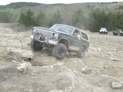 1986 Ford Bronco - Ford Bronco navigating a challenging rocky off-road course with other vehicles present.