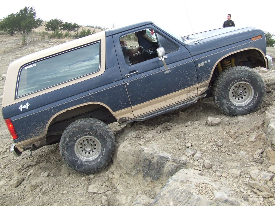 Blue and tan Ford Bronco with off-road tires climbing rocks