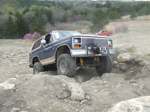 1986 Ford Bronco - This 1986 Ford Bronco navigates a rocky trail, equipped with a front-mounted winch for off-road challenges.