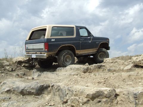 1986 Ford Bronco - 1986 Ford Bronco climbing over rocks on an off-road trail.