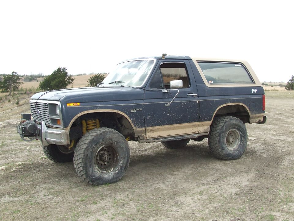 Dark blue Ford Bronco with tan trim, lifted suspension, and winch, parked on dirt