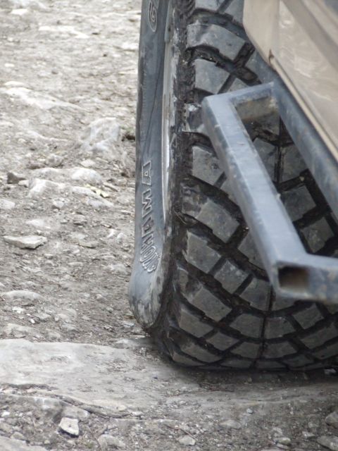 1986 Ford Bronco - Close-up of an off-road tire and a metal rock slider on a rocky surface.