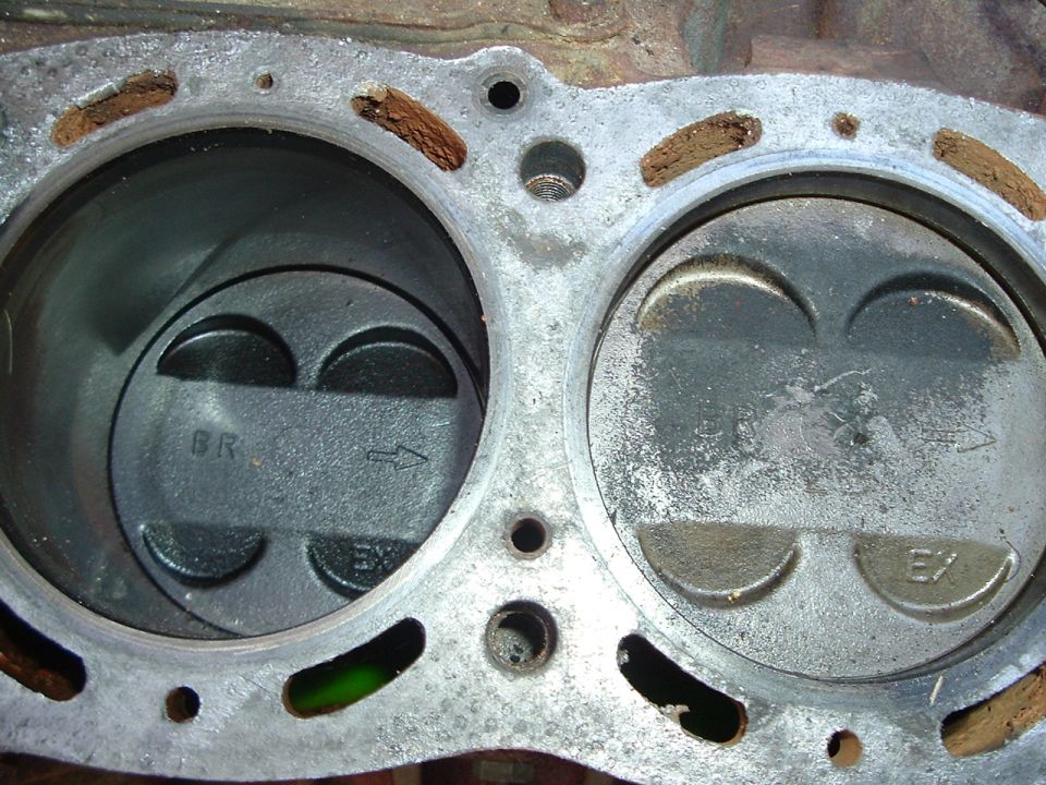 Engine block with two pistons, one marked BR, the other EX. Rusty gasket material visible