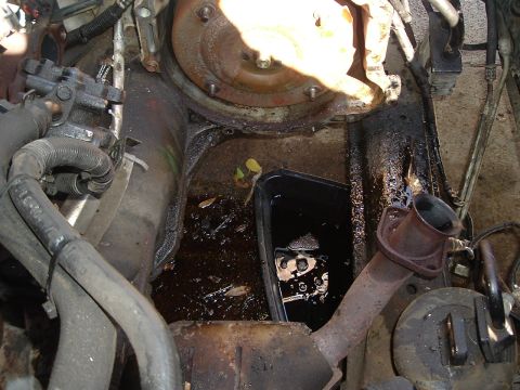 1993 Ford Taurus - The engine bay shows a messy oil spill collected in a black pan, with parts of the transmission and exhaust visible.