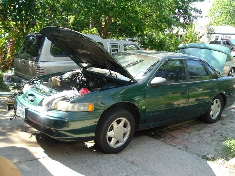 1993 Ford Taurus - A green sedan with its hood open is parked in a driveway next to a pickup truck.