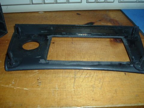 1993 Ford Taurus - A black plastic car interior trim piece with a rectangular cutout and a circular hole is shown on a wooden surface.