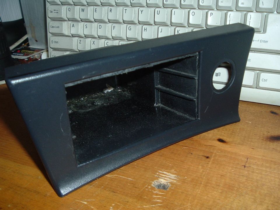 Dark gray center console trim piece with storage cubbies and a circular cutout