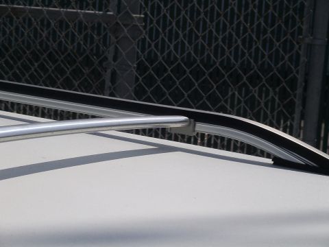 1993 Ford C-350 (Centurion Conversions) - Detail of a vehicle roof rack rail and trim against a chain-link fence background.