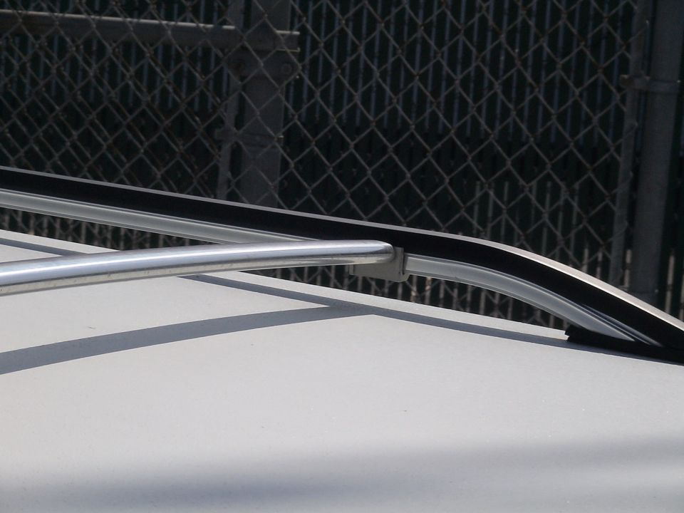 Close-up of a silver roof rack rail with black trim attached to a light-colored surface