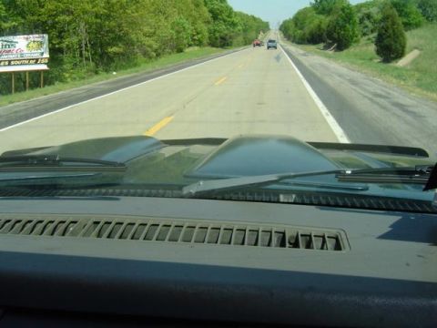 1979 Ford Bronco - View from inside a vehicle with a green dashboard and hood, driving on a highway with other cars in the distance.
