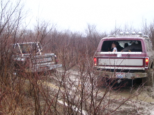 Maroon 1978 Ford Bronco with diamond plate tailgate insert, seen from rear in muddy terrain with another vehicle partially visible
