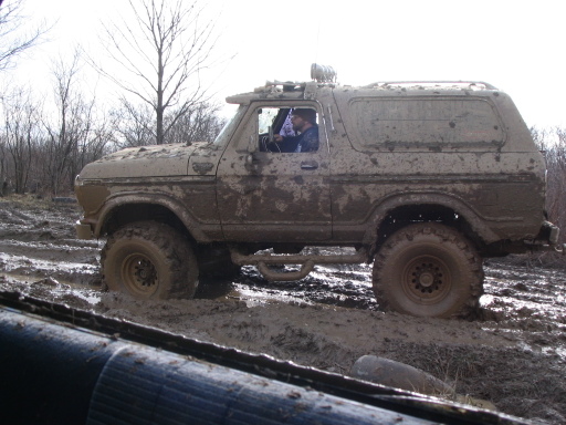 Muddy SUV stuck in a muddy trail, driver visible inside
