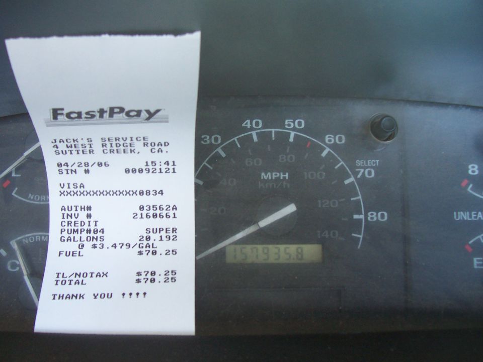 Fuel receipt held over truck gauge cluster showing 157,935 miles on the odometer