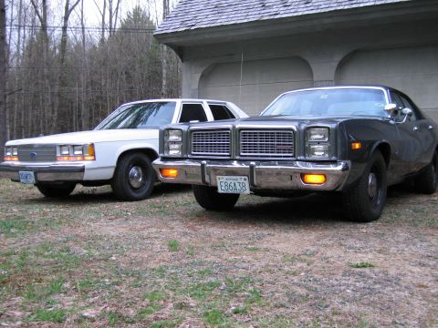 1991 Ford LTD Crown Victoria - Two sedans are parked in front of a garage, with the front vehicle being a dark color and the rear vehicle being white.