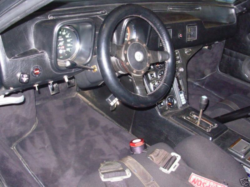 Black sports car interior with three-spoke steering wheel, gauges and console shifter