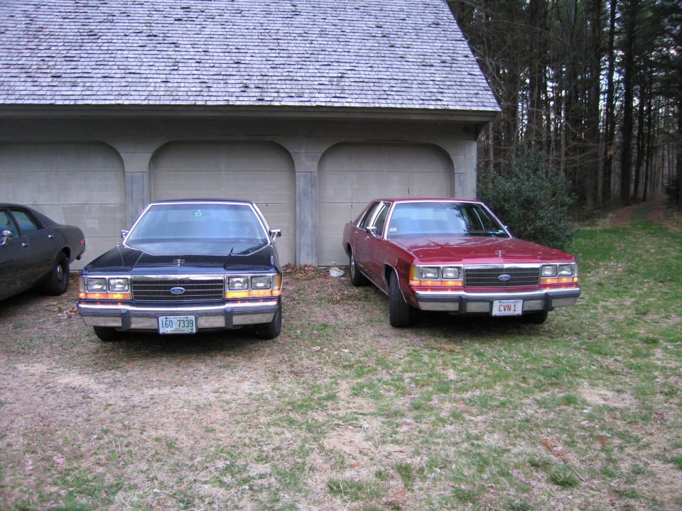 Two Ford Crown Victorias parked in front of a garage, one black and one red