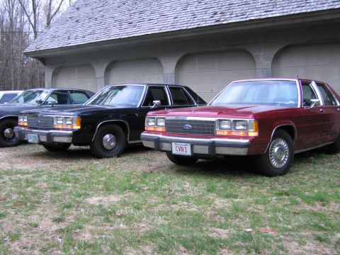 1991 Ford LTD Crown Victoria - Three Ford Crown Victorias are parked in front of a garage, with the closest vehicle being red.