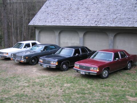 1991 Ford LTD Crown Victoria - Four sedans, including a maroon 1991 Ford Crown Victoria LTD, are parked in front of a garage.