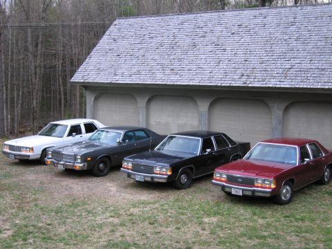 1991 Ford LTD Crown Victoria - Four sedans are parked in front of a garage with a shingled roof.