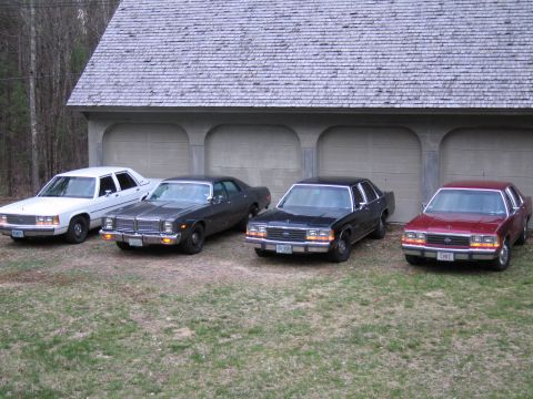 1991 Ford LTD Crown Victoria - Four sedans are parked in a row in front of a garage with a shingled roof.