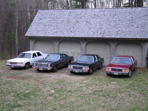 1991 Ford LTD Crown Victoria - Four sedans are parked in front of a garage, with the white 1991 Ford Crown Victoria LTD on the far left.