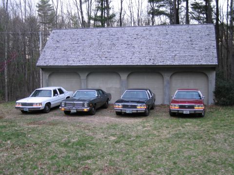 1991 Ford LTD Crown Victoria - Four sedans, including a red 1991 Ford Crown Victoria LTD, are parked in front of a multi-bay garage.