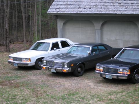 1991 Ford LTD Crown Victoria - Three sedans are parked in front of a garage. The middle car is a 1977 Dodge Monaco, and the car on the right appears to be a Ford Crown Vi…