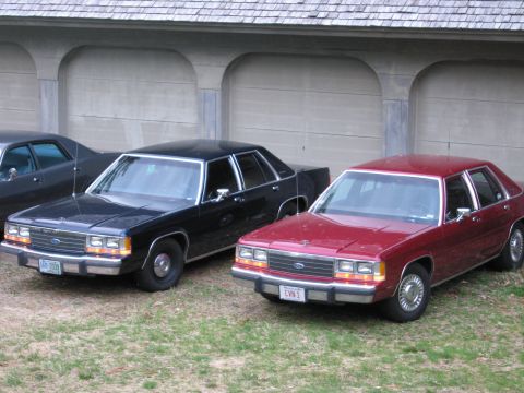 1991 Ford LTD Crown Victoria - Two Ford Crown Victorias are parked side-by-side in front of a garage.