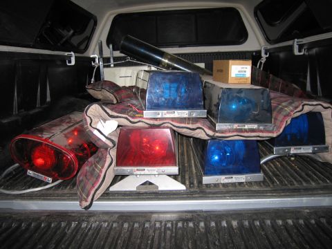 1991 Ford LTD Crown Victoria - Several red and blue rotating emergency beacon lightbars and a black spotlight laid out on a plaid blanket in a pickup bed at night.
