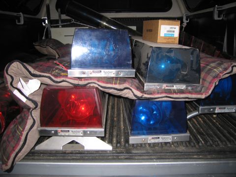 1991 Ford LTD Crown Victoria - Federal Twin Sonic red and blue rotating emergency beacons sit on a plaid blanket in a pickup bed with a cardboard box behind them.