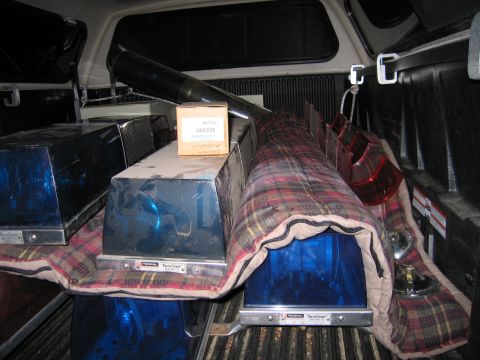 1991 Ford LTD Crown Victoria - Multiple blue and red emergency lightbars and a black spotlight are stacked on plaid blankets in a pickup truck bed at night.