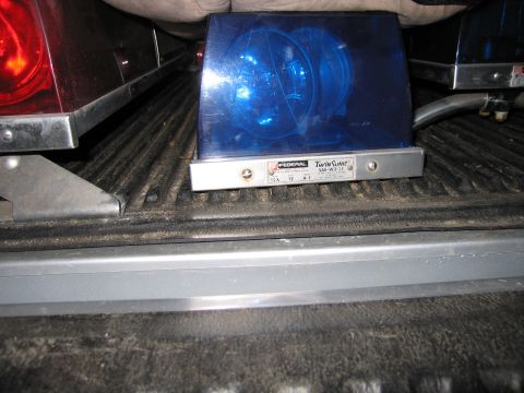 1991 Ford LTD Crown Victoria - Federal Twin Sonic blue rotating emergency beacon light with its silver base sits on an open pickup tailgate.