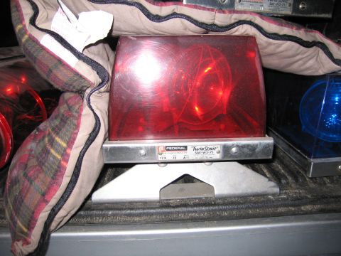 1991 Ford LTD Crown Victoria - Federal Twin Sonic red rotating emergency beacon light sits on a metal stand among blankets and other beacons in a truck bed.